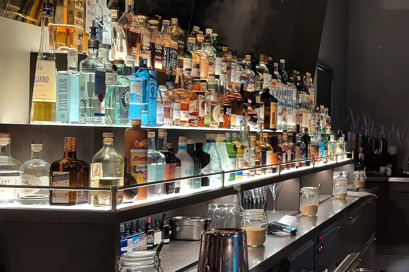 Backbar der Boilerman Bar mit beleuchteten Flaschenregalen und gestapelten Rührgläsern