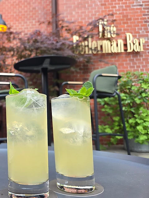 Zwei Highballs mit Minze auf einem Tisch vor der Backsteinwand mit dem Schriftzug The Boilerman Bar