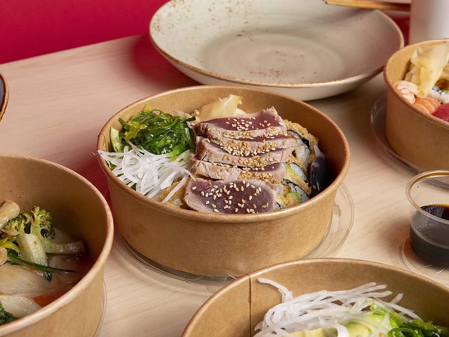 Bowls mit Thunfisch-Tataki, Salat und Gemüse auf einem Holztisch, dazu Sojasauce