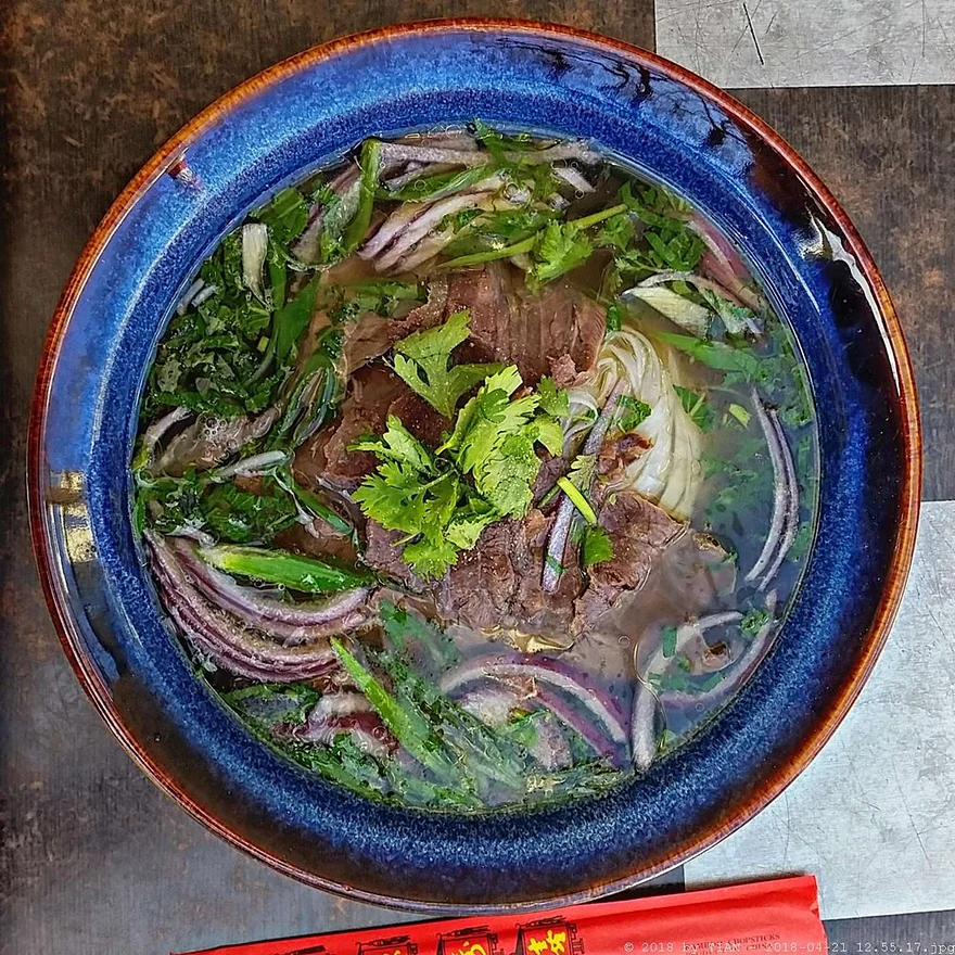 Phở mit Rindfleisch, Reisnudeln, Zwiebeln und Koriander in blauer Schale