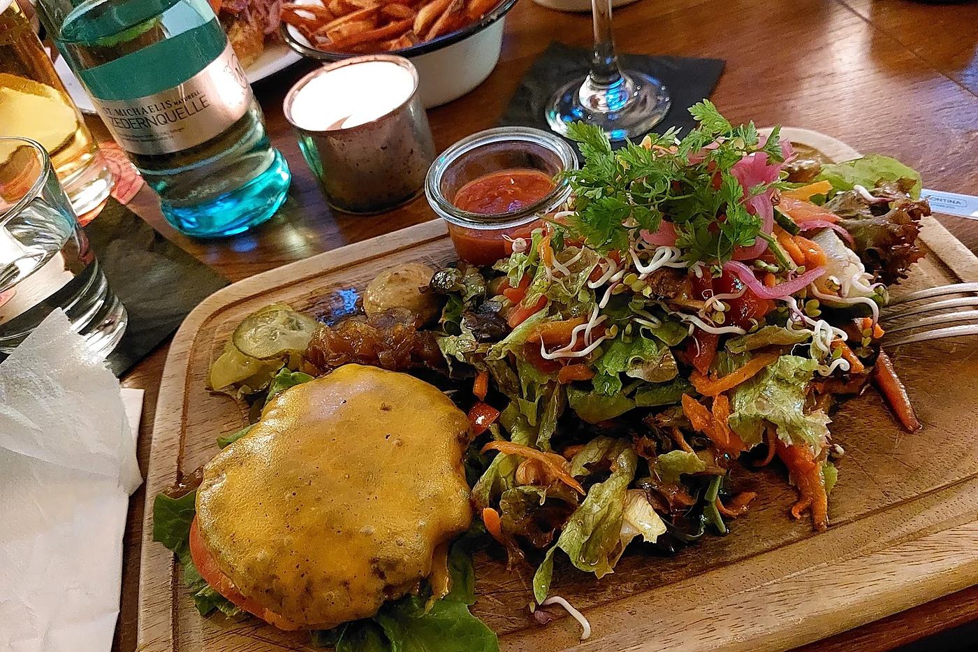 Burger mit geschmolzenem Käse und großem Salat auf einem Holzbrett, dazu Süßkartoffelpommes