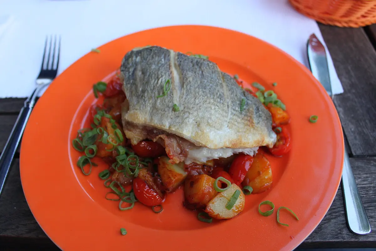 Gebratenes Fischfilet mit knuspriger Haut auf Bratkartoffeln mit Tomaten und Frühlingszwiebeln