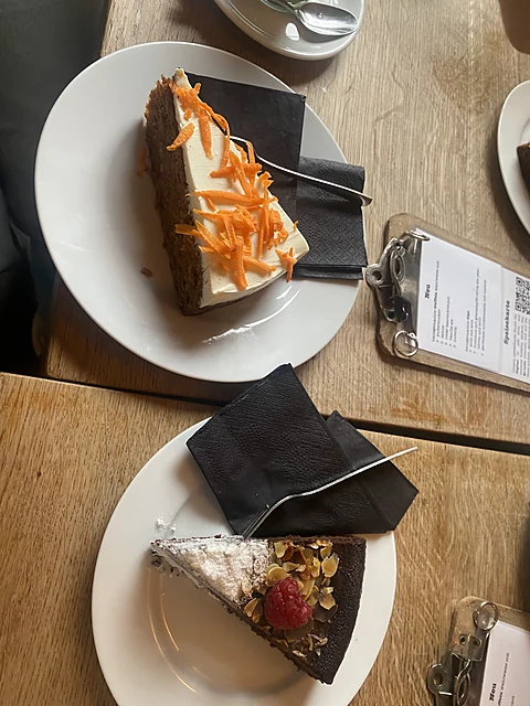 Zwei Kuchenstücke auf weißen Tellern: Karottenkuchen mit Frischkäsecreme und Möhrenstreifen sowie Schokoladenkuchen mit 