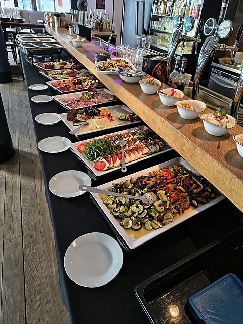 Langes Brunchbuffet mit vielen Platten und Schalen entlang der Bar, davor gestapelte Teller