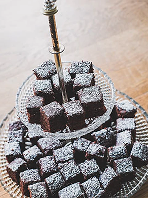 Brownie-Würfel mit Puderzucker auf einer gläsernen Etagere auf Holztisch