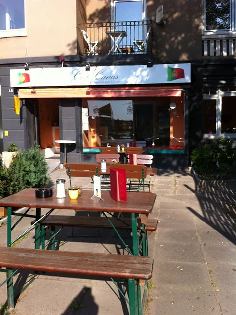 Terrasse des Café Canas mit Bierbänken und Holztischen vor der orangefarbenen Ladenfront