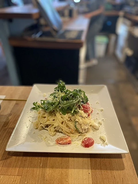 Weißer eckiger Teller mit Pasta in heller Sauce, Kirschtomaten und frischem Rucola auf dem Tresen des Bistros