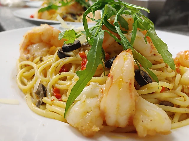 Spaghetti mit Garnelen, Oliven, Chili und Rucola auf einem weißen Teller