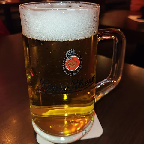 Frisch gezapftes Pils mit hoher Schaumkrone in einem Glaskrug auf dunklem Tisch