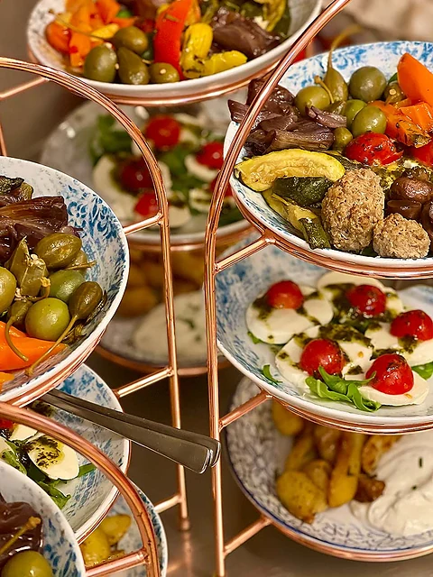 Kupferfarbene Etagère mit Schälchen voller Oliven, Antipasti-Gemüse, Hackbällchen, Caprese und Bratkartoffeln