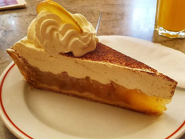 Stück Sahnetorte mit Kakaostaub, Sahnetupfer und Apfelscheibe auf einem Teller mit rotem Rand