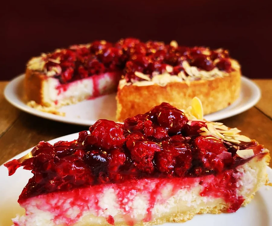 Angeschnittene Torte mit Kirschen, Sahnecreme und Mandelblättchen auf weißem Teller