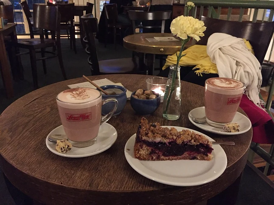 Stück Streuselkuchen mit Beeren und zwei Milchkaffee auf rundem Holztisch