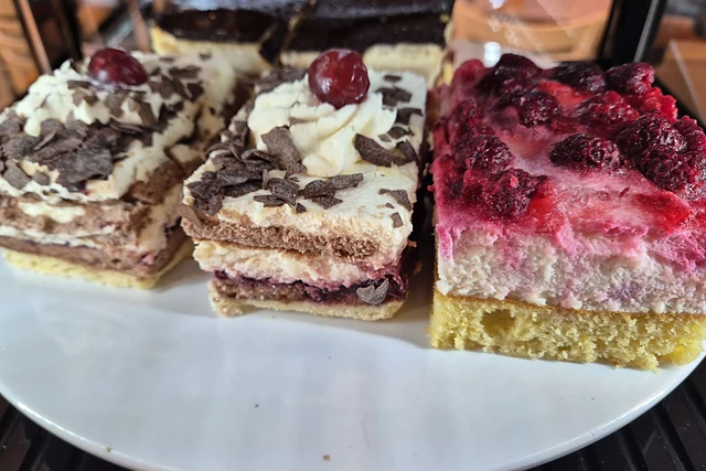 Drei Stücke Blechkuchen auf einem weißen Teller: Kirsch-Sahne, Schoko-Sahne und Himbeer-Quark