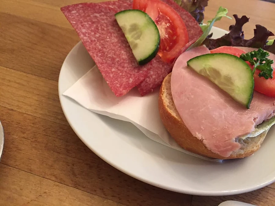 Belegte Brötchen mit Schinken, Salami, Gurke und Tomate auf weißem Teller