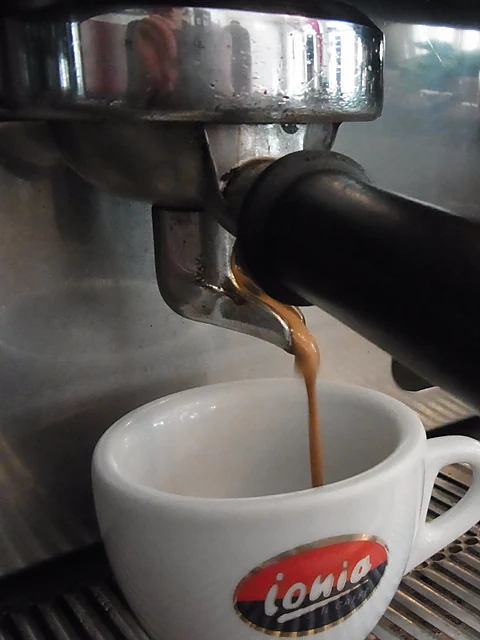 Espresso läuft aus dem Siebträger einer Espressomaschine in eine weiße Tasse mit rotem Ionia-Logo