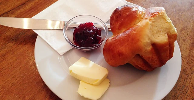 Frisch gebackene Brioche mit Butter und einem Schälchen Beerenmarmelade auf einem weißen Teller