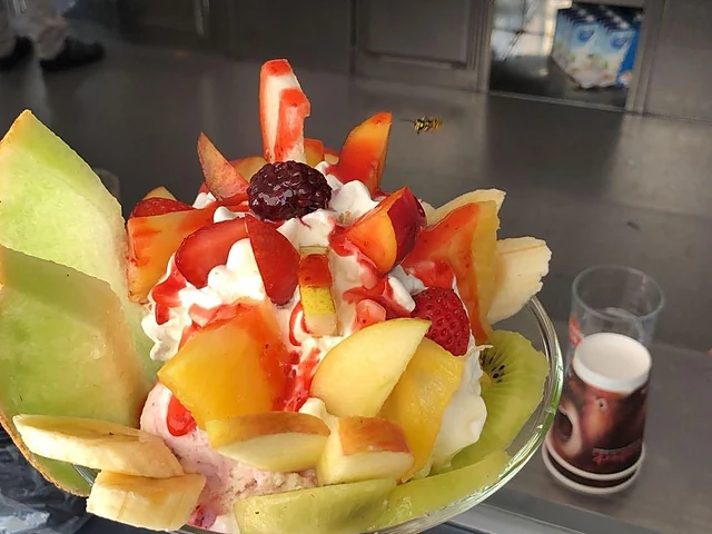 Eisbecher mit frischen Früchten, Melone, Kiwi, Erdbeeren, Banane und Sahne in einer Glasschale