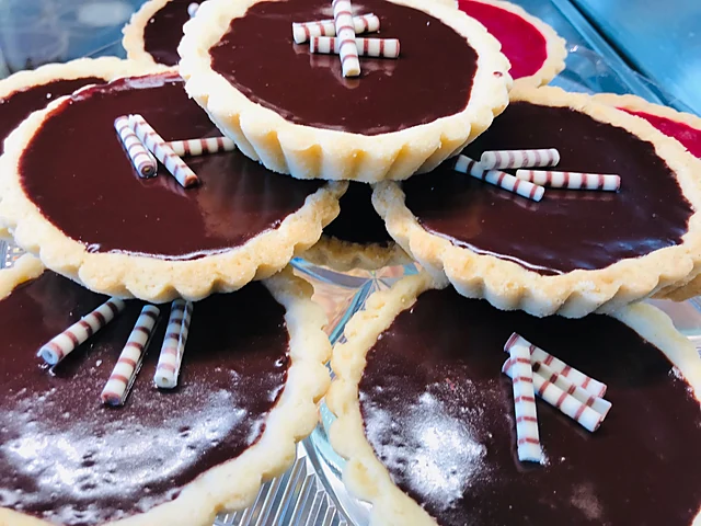 Mehrere Schokoladentartelettes mit glänzender Ganache und gestreiften Waffelröllchen auf einer Glasplatte
