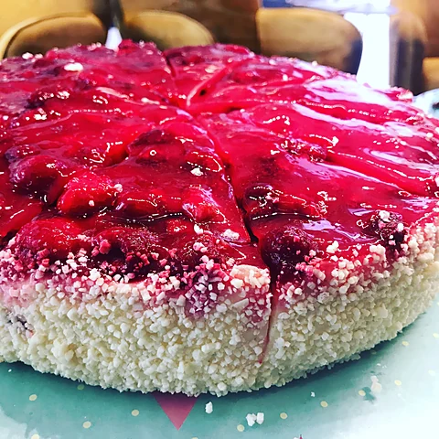 Angeschnittener Kuchen mit leuchtend roter Beerenglasur und Streuselrand auf einem Tortenteller