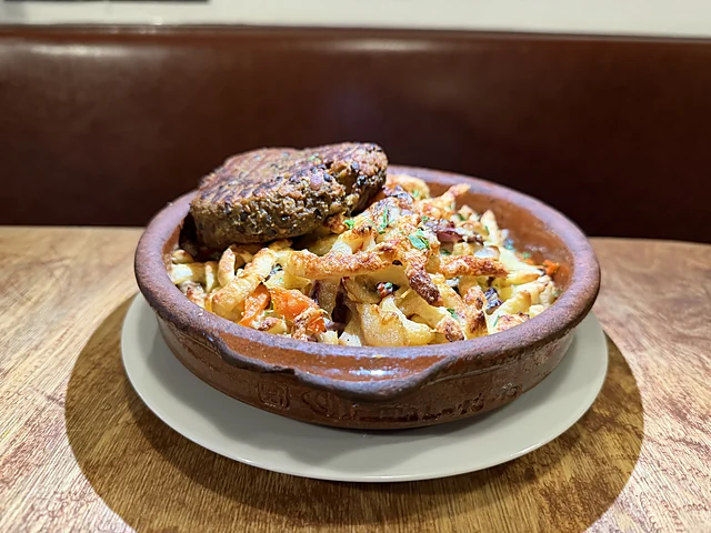 Tonschale mit Nudeln in Tomatensauce, obenauf eine Frikadelle, auf einem Holztisch vor einer Lederbank