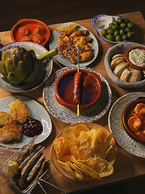 Tapas-Tafel von oben: Artischocke, Chorizo in Tonschale, Garnelen, Kroketten, Chips, Oliven, Brot und Aioli