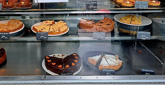 Vitrine mit Tartes, Törtchen und angeschnittenen Kuchen auf Tortenplatten mit kleinen Preisschildern