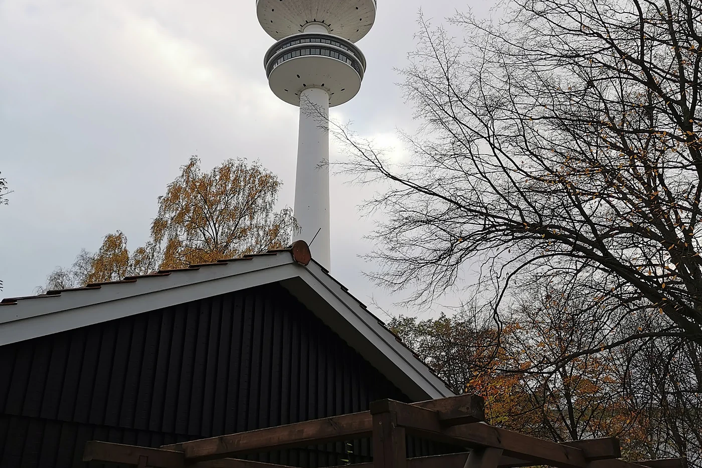 Der Heinrich-Hertz-Turm ragt hinter dem dunklen Holzdach des Schrødingers in den grauen Himmel, davor kahle Bäume
