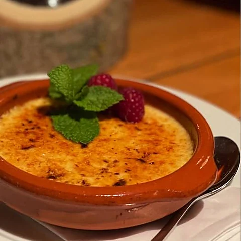Crème brûlée in brauner Tonschale mit Himbeeren und Minze, dahinter ein Windlicht