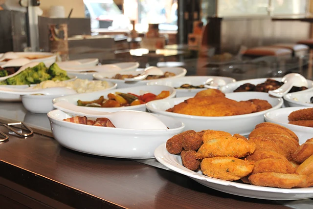 Buffet mit weißen Schalen voller Antipasti, Gemüse, Schnitzel und einem Teller Kroketten und Pastéis