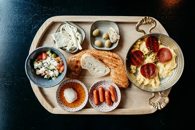Holztablett mit Rührei und Sucuk in der Pfanne, Weichkäse, Oliven, Salat, Kajmak, Würstchen und Simit