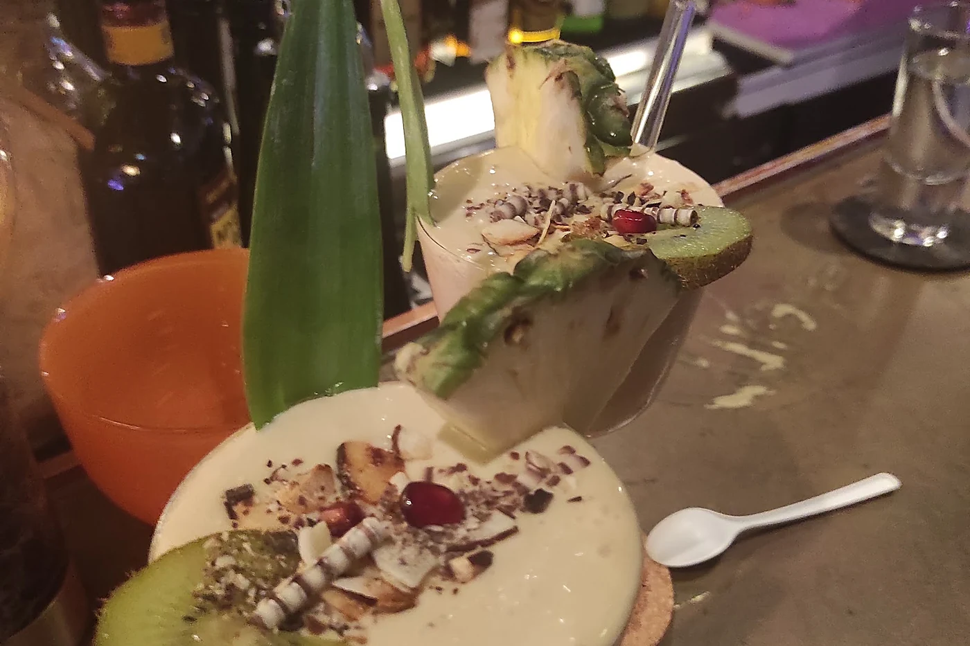 Cremiger Cocktail im Kokosnuss-Stil mit Ananasstück, Kiwi und Kokosraspeln auf dem Tresen