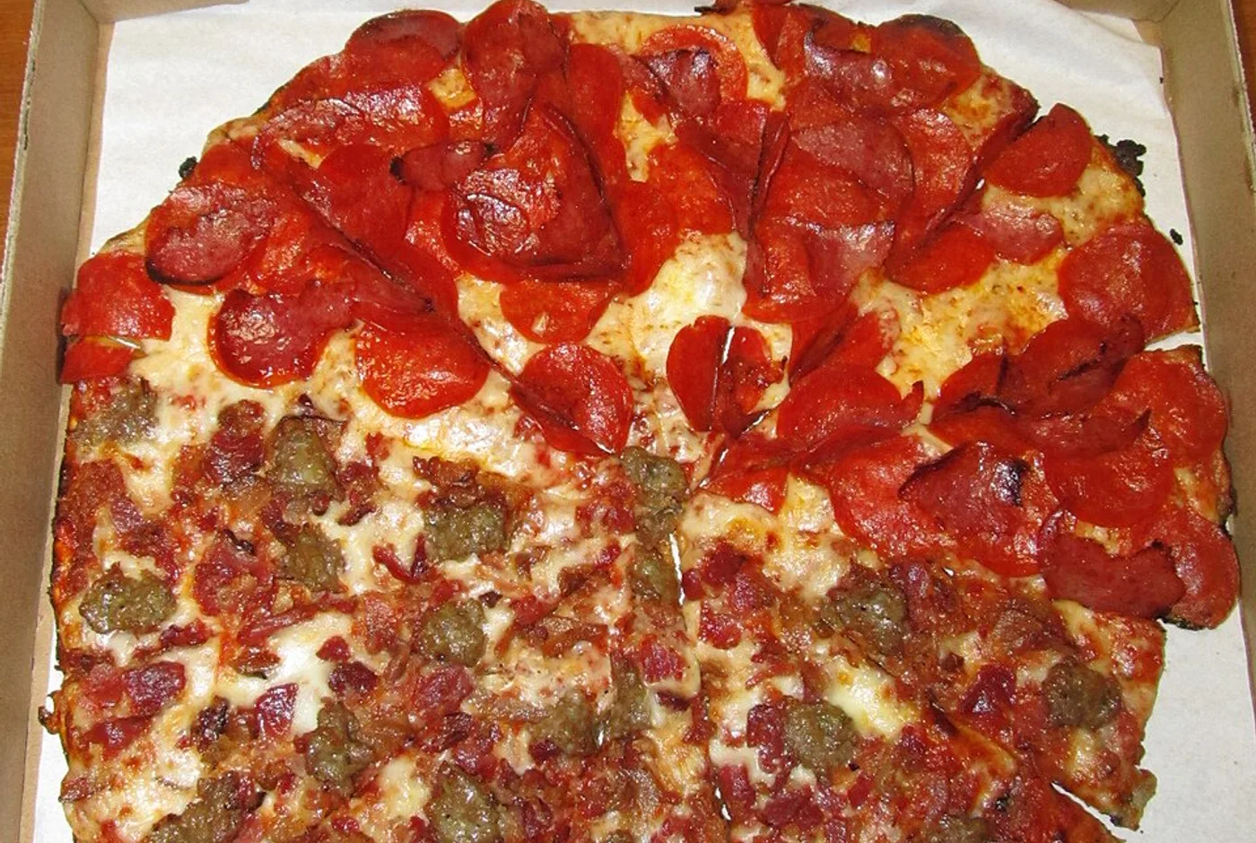 Geschnittene Pizza mit Salami und Hackfleisch in einem geöffneten Lieferkarton