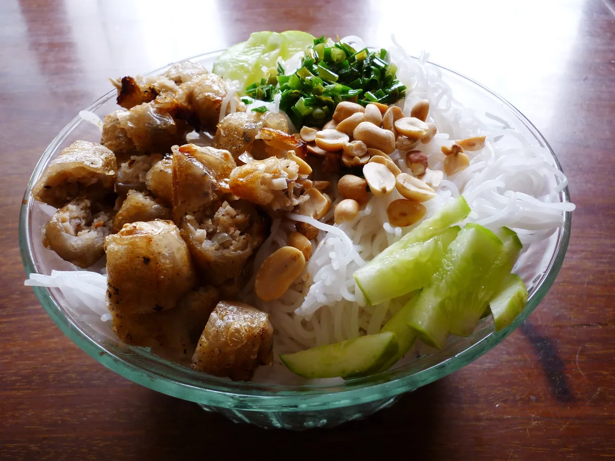 Schale mit Reisnudeln, angeschnittenen Frühlingsrollen, Erdnüssen, Gurke und Frühlingszwiebeln