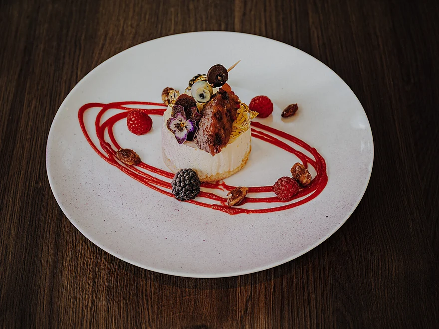 Dessert mit Cheesecake-Törtchen, Beeren, essbaren Blüten und Fruchtspiegel