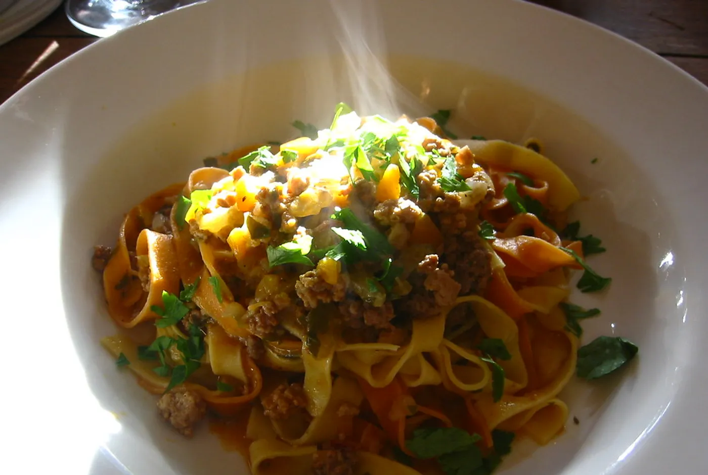 Tagliatelle mit Fleischsauce und Kräutern in einem tiefen weißen Teller