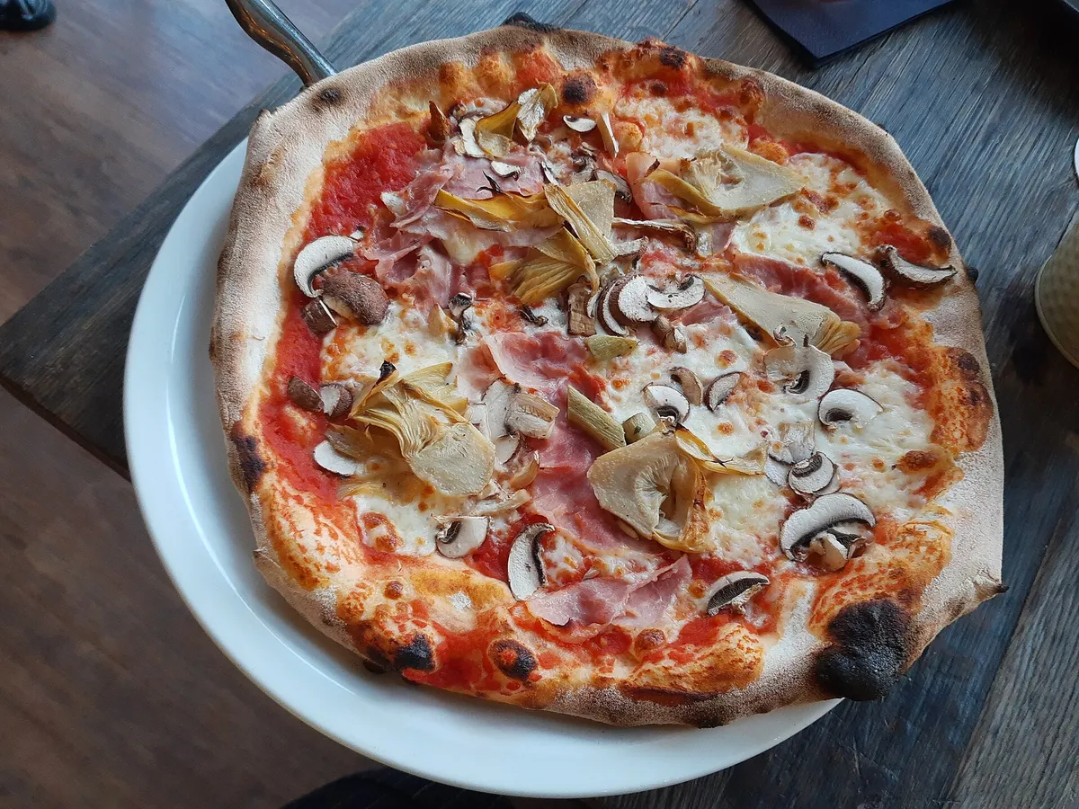 Pizza mit Schinken, Champignons und Artischocken auf einem weißen Teller
