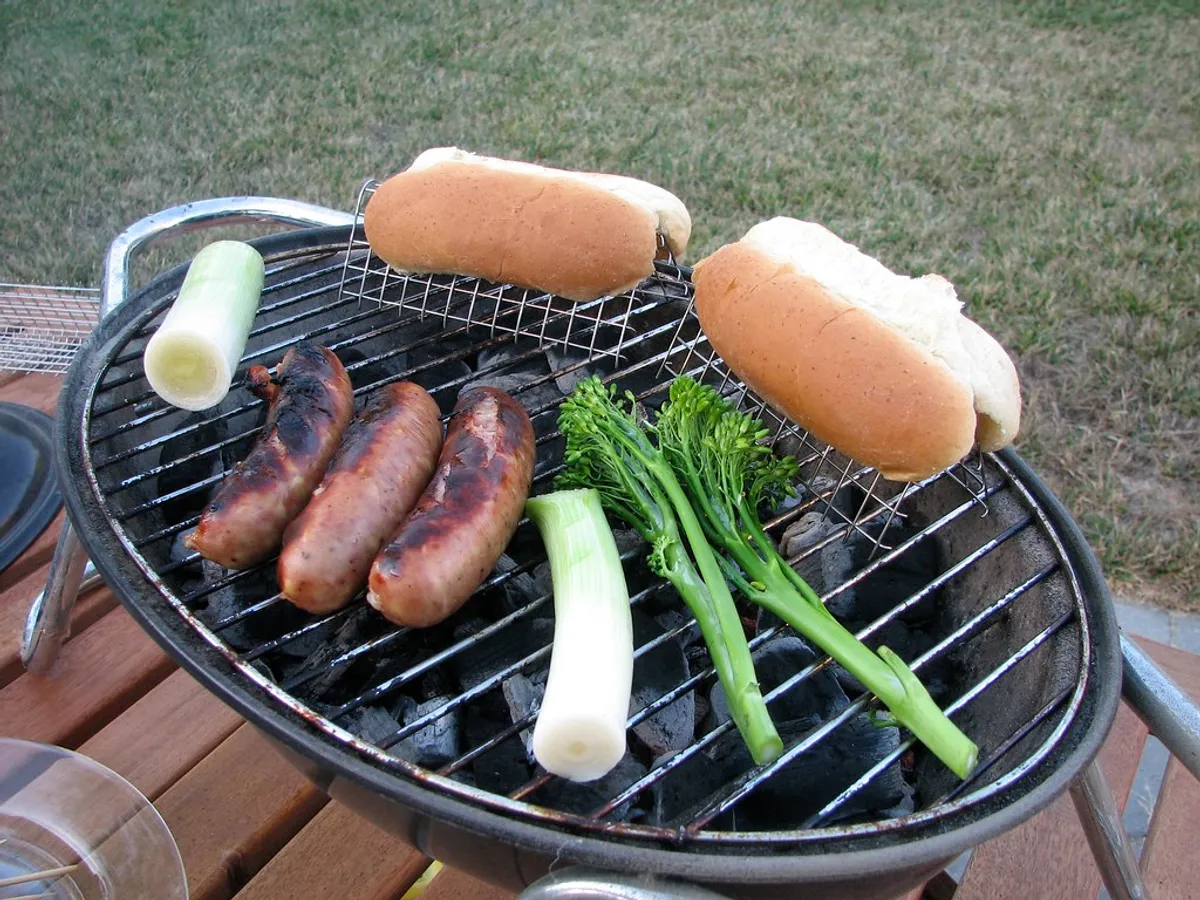 Kleiner Rundgrill mit Würstchen, Brötchen und Gemüse im Freien