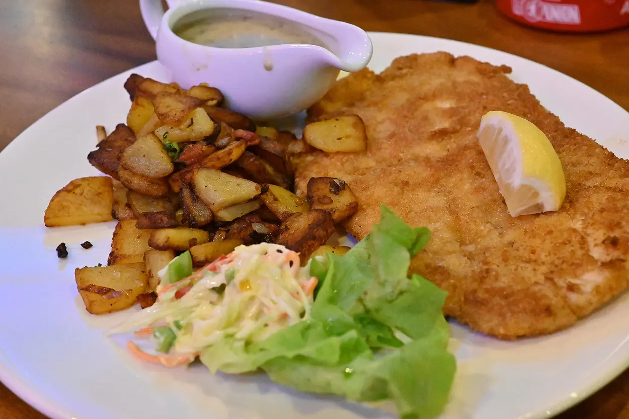 Großes paniertes Schnitzel mit Zitrone, Bratkartoffeln, Krautsalat und Sauce