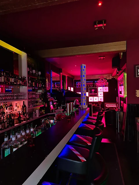 Langer Bartresen der 24 Carat mit Barhockern, Flaschenregal und blauem und pinkem Neonlicht