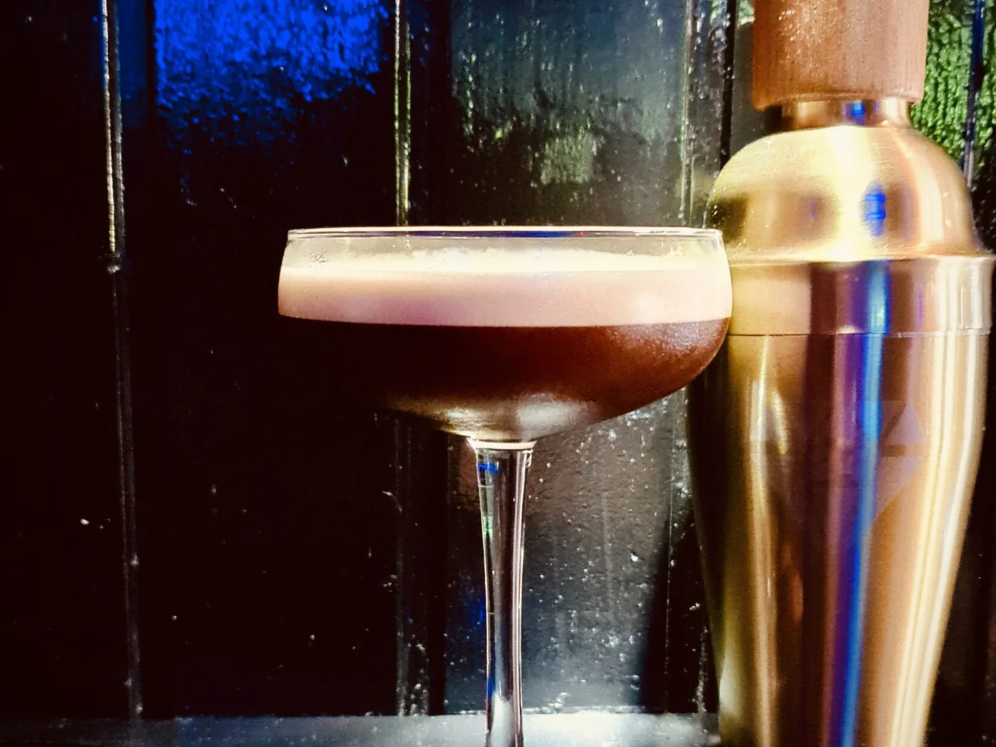 Espresso Martini neben einem Cocktailshaker vor blauem Licht