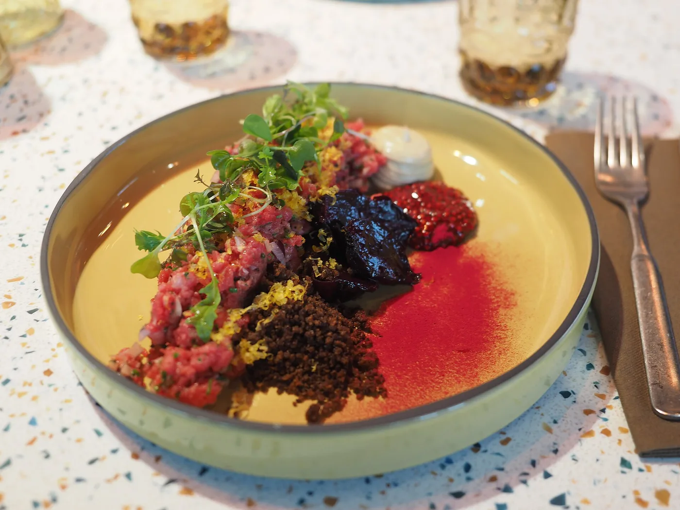 Steak Tartare mit Kräutern, Roter Bete und Krokant auf einem gelben Teller