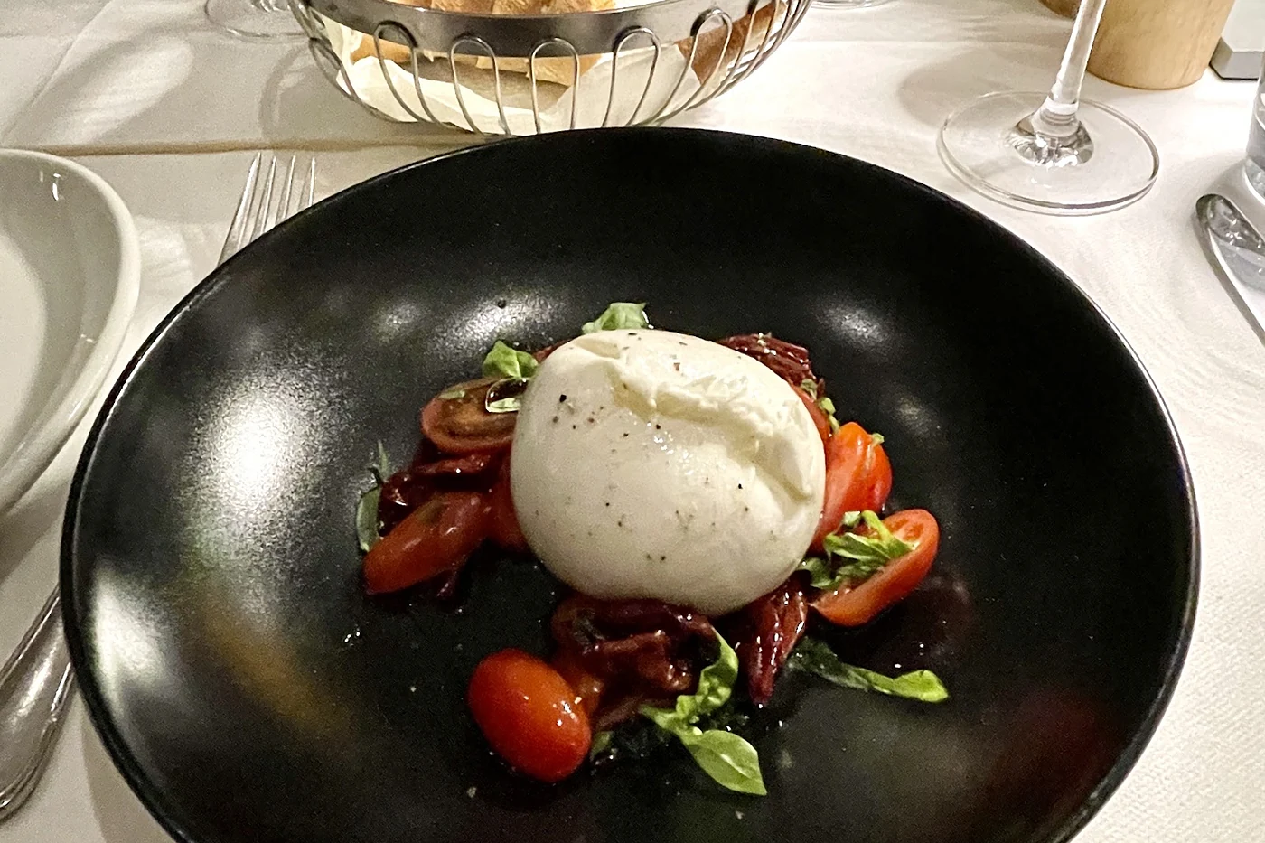 Burrata mit Tomaten und Kräutern in einer schwarzen Schale