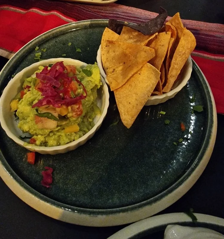 Guacamole mit eingelegten roten Zwiebeln in einer Schale, daneben frittierte Maischips