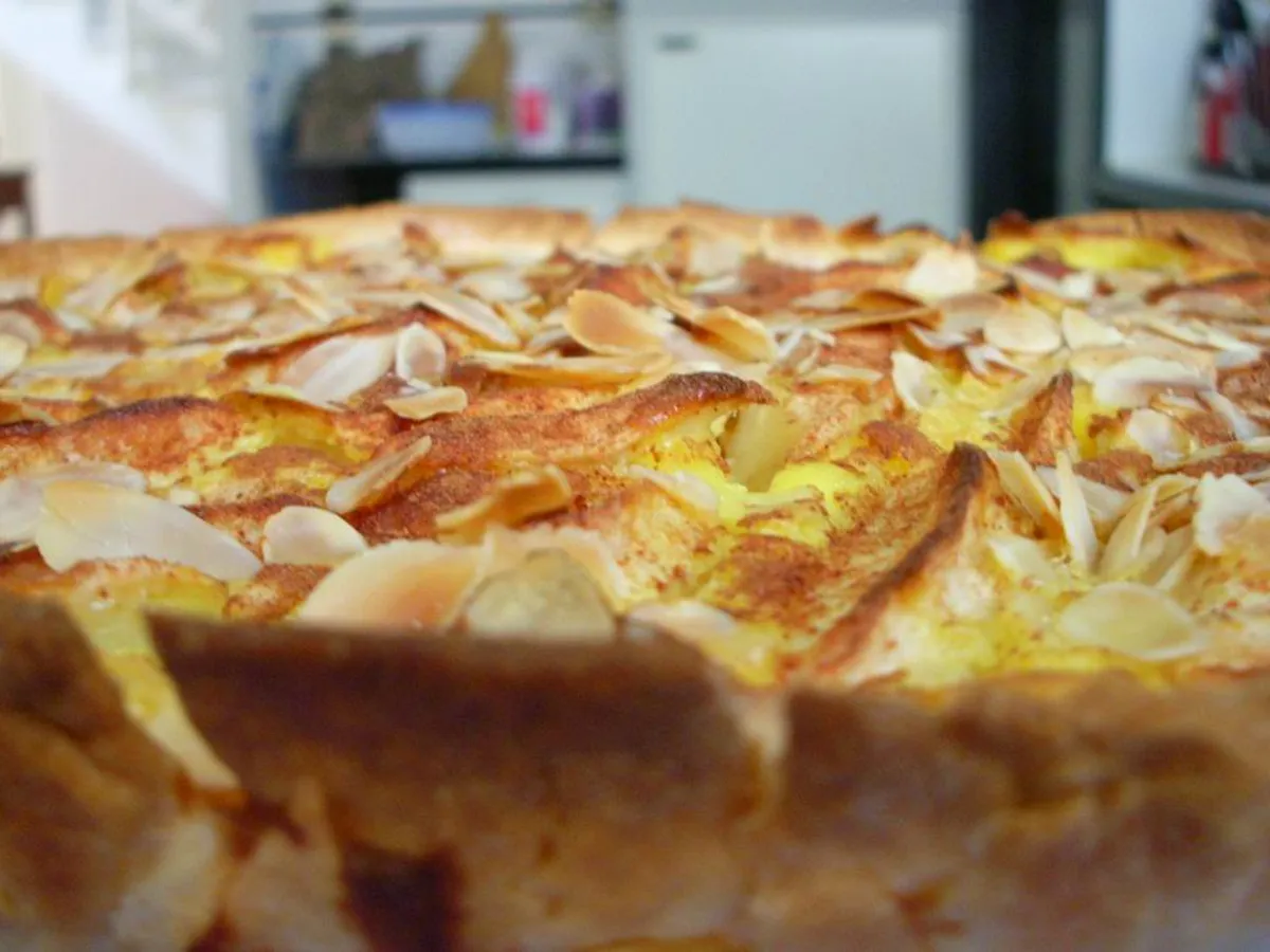 Apfelkuchen mit Mandelblättchen auf einem Blech, ein Stück ist herausgeschnitten