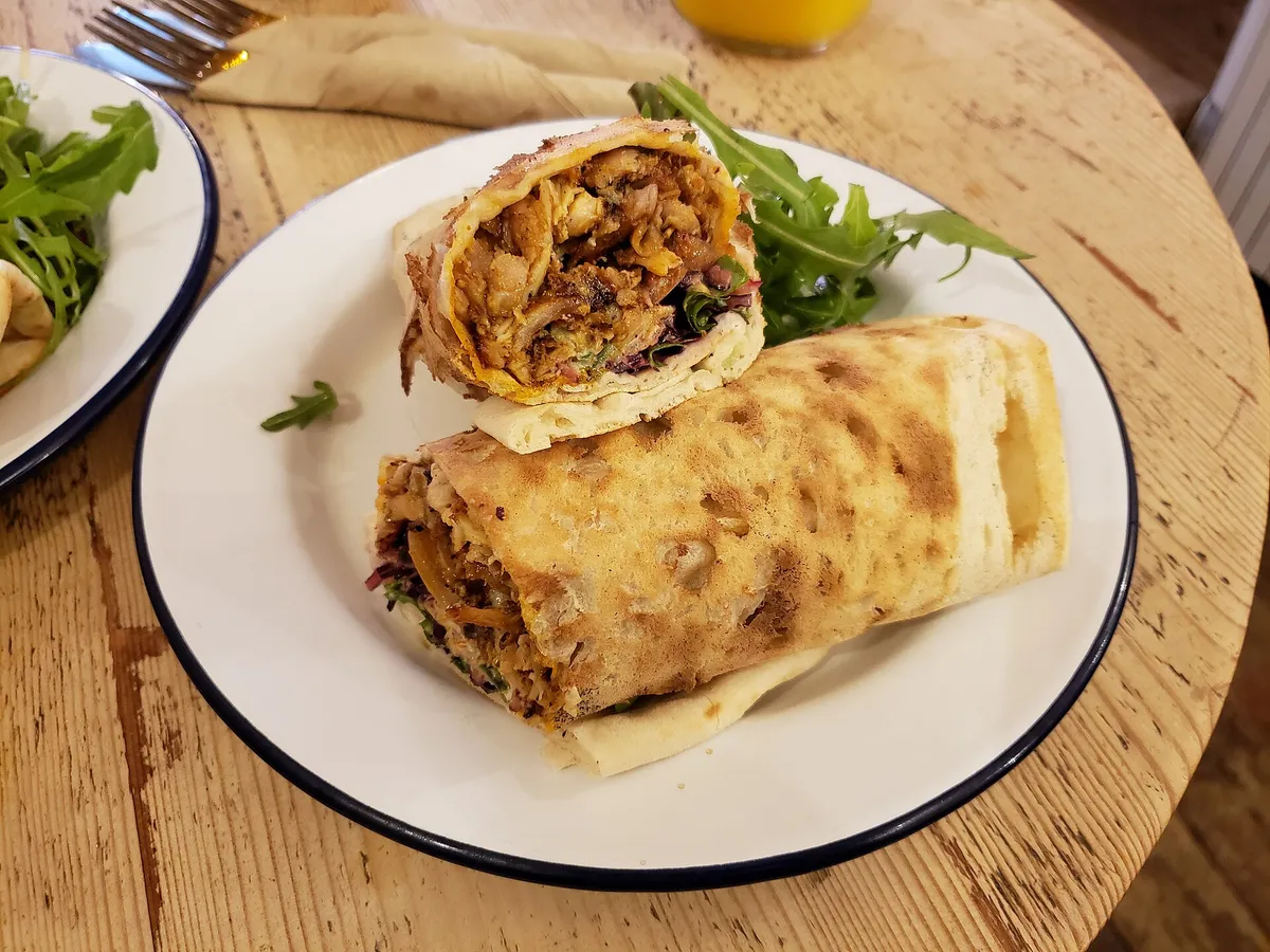 Halbierter Wrap mit Hähnchenfüllung auf einem Teller, daneben Rucola