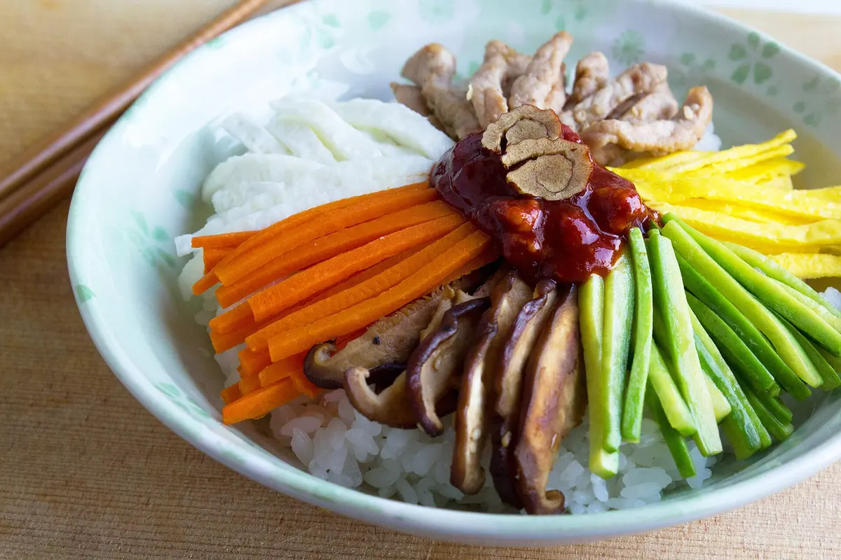 Bibimbap in einer Schale mit Reis, Karotten, Gurke, Pilzen und Fleisch
