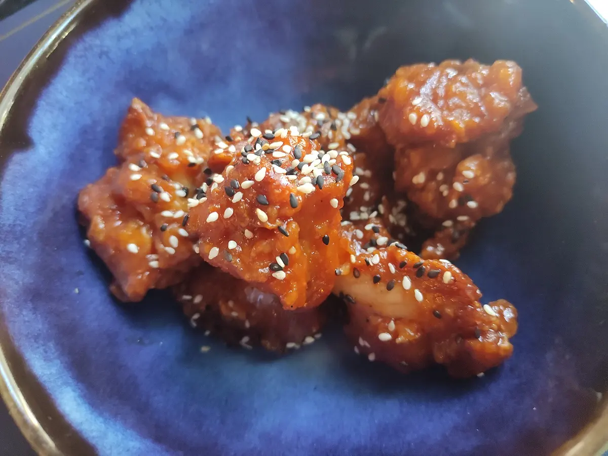 Frittierte Hähnchenstücke in roter Sauce mit hellen und schwarzen Sesamkörnern