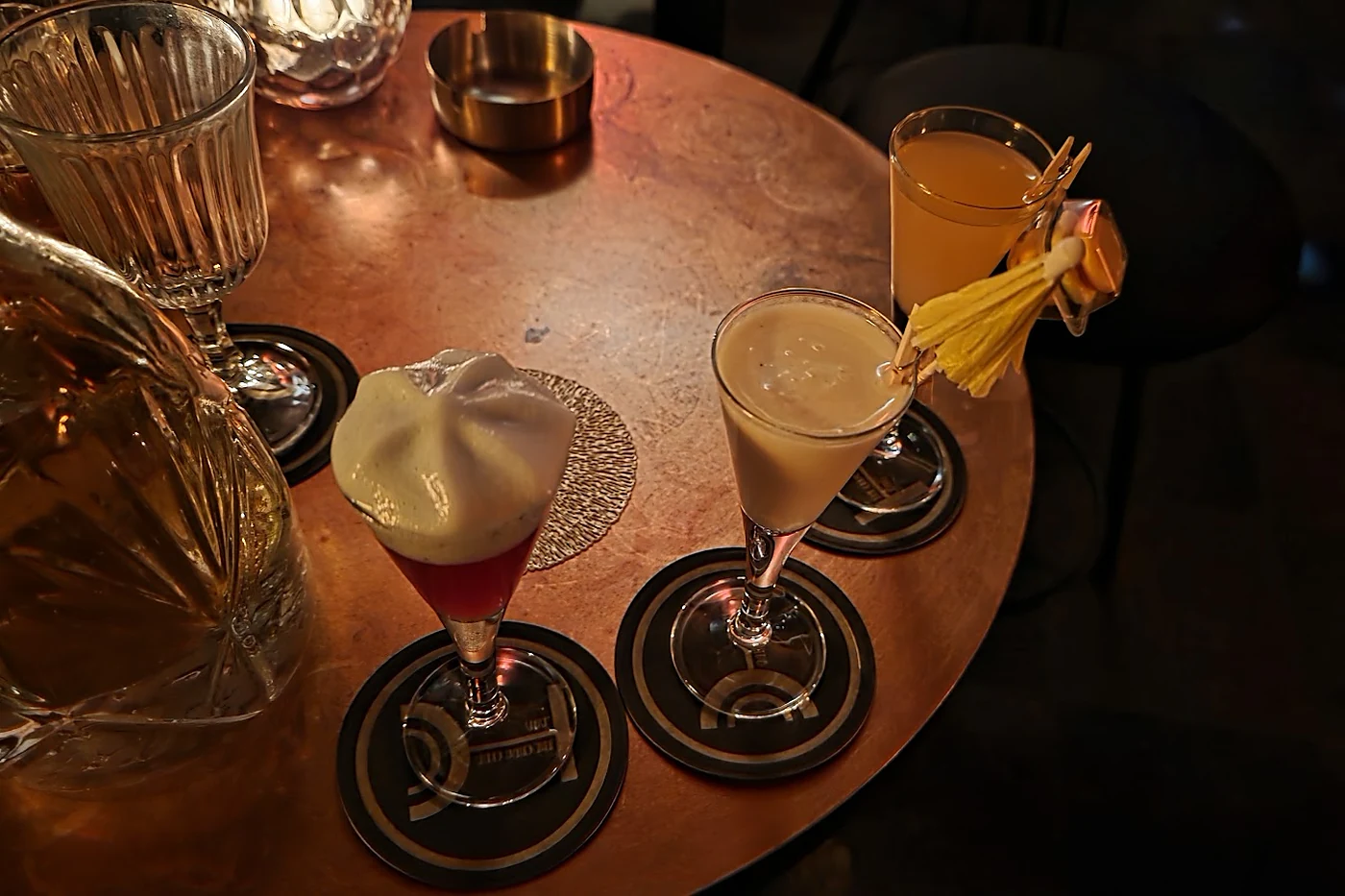 Drei Chugs in kleinen Stielgläsern auf bedruckten Untersetzern auf einem Kupfertisch im Chug Club