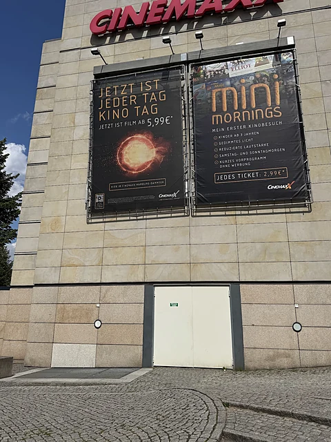 Helle Natursteinfassade mit rotem CINEMAXX-Schriftzug und zwei großen Filmplakaten